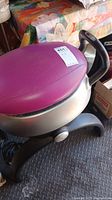 Photo showing the purple padded seat, one handlebar and part of the base frame with the lot tag.