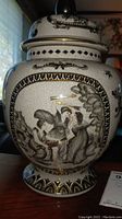Front view of the ginger jar showing classical figures in black and gold on a crackle glaze ceramic body.