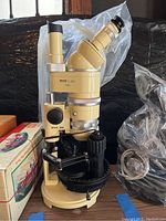 Full view of beige Wild Heerbrugg stereo microscope on wooden table showing angled binocular head, rotating stage, power cable