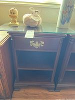 Front view of wooden nightstand showing one drawer with ornate brass handle and two open shelves below.