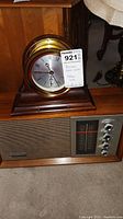 Color photo showing both the Panasonic AM/FM radio with wooden cabinet and Chelsea mantel clock with brass case on top.