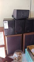 Stacked view showing two wood-grille speakers at bottom and three black bookshelf speakers above, plus one angled speaker on top.