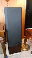 Front view of one speaker with grille attached, positioned beside lamp and table