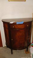 Front view of half moon shaped mahogany entry table with drawer and cabinet door closed