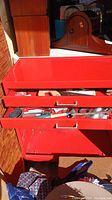 Photo showing the red metal tool box with drawers open revealing assorted hand tools such as handsaws, pliers, and a hammer.