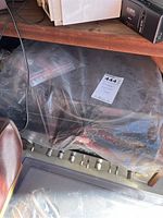 Plastic-wrapped items under shelf showing partially visible Sony receiver front panel with wooden trim and multiple control knobs.