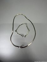 Two sterling silver chains, one longer laid in a circular shape and one shorter, displayed on a plain surface.