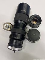 Photo showing three vintage camera lenses including a large telephoto lens marked Z-215304 made in Japan, a Pentax Takumar lens, and another lens with PK marking. Visible lens mount and focus markings.