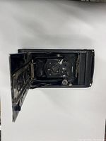 Front open view of the vintage folding camera showing bellows, lens, shutter speed dial, and mechanical lever.