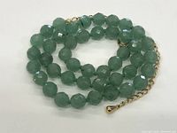 Close-up image showing faceted round green beads of a vintage necklace and gold-tone adjustable chain clasp.