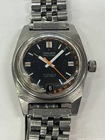 Close up photo of the Gruen Precision wristwatch showing black dial with white and orange markers, 17 jewels and 200 feet water resistance text, date window at 6, stainless steel case and metal bracelet with visible scratches.