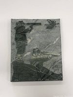 Full view of the Inuit stone carving plaque showing two hunters aiming rifles at a bird, mounted on a natural textured stone surface.