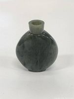 Front view of the polished jade bottle showing its rounded flat shape and cylindrical neck opening.