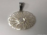 Front view of the oval mother of pearl pendant showing the carved flower petal design and polished oval centerpiece with decorative silver bail.