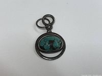 Close-up image of the pendant showing the turquoise stone and antique silver frame with dual loops for attachment.
