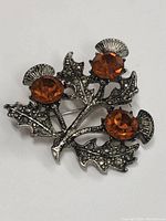 Front view of the Scottish thistle brooch pin showing three amber-colored stones set in textured silver-tone metal leaves and thistle tops.