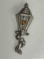 Photo showing the front view of the Scottish sterling silver brooch shaped like a lamp post with a citrine gemstone set in the lantern center.