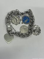 Photo of sterling silver charm bracelet laid out flat showing all 5 charms and heart tag