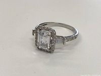 Front angle showing large rectangular center stone with small halo stones and stones along band.