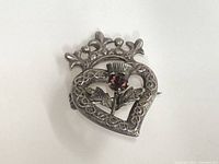 Front view of the sterling silver pin showing heart shape, Celtic knots, amethyst thistle flower, and crown