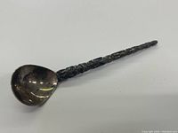 Angled side view of tarnished spoon showing bowl and totem pole handle.