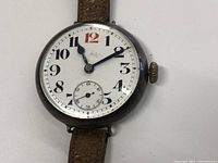 Close-up front view of white enamel dial with black Arabic numerals, red 12, blued steel hands, subsidiary seconds dial.