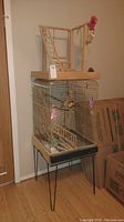 Full view showing the metal bird cage on a stand with hairpin legs and the wooden bird playground on top.