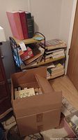 Books stacked on a vintage bookshelf and in a cardboard box on the floor