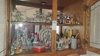 Two glass cabinet shelves filled with miniature ceramic tea sets, glass goblets, salt and pepper shakers, and other decorative kitchenware items