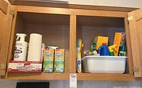 Cabinet containing several cleaning items including paper towels, Arm & Hammer carpet odor eliminator boxes, and other assorted products