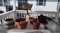 Photo showing seven planters of various materials and sizes arranged on a glass outdoor table on a balcony. Planters include ceramic, plastic, metal, and wicker basket stand.