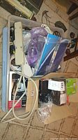 Plastic tub filled with assorted extension cords, power cords, older cell phones, cordless phones, and other electronic accessories, packed together inside a clear plastic tub on carpet.