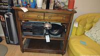 Front view of wooden bookshelf showing two shelves with radio equipment inside, drawer with brass ring pulls and pull-out writing surfaces.