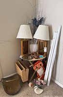 Wide view of the corner showing the TV tray with lampshades on top, white vase with dried blue and white flowers, a wooden magazine rack, a brass log holder, and various decorative items on and around the tray.
