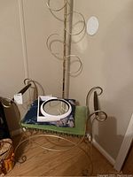 Vanity stool with blue cushion and green fabric, small round mirror resting on stool, tall brass towel rack behind