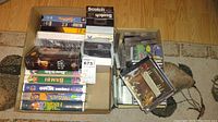 Two boxes filled with VHS tapes showing various titles and some CDs and cassette tapes in cases.
