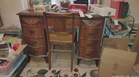 Front view of the vintage mahogany desk with nine drawers and stack of various items on top, with matching chair pushed under desk