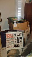 Photo showing a box containing numerous vinyl records and some album covers visible including 'Top Hits Top Stars'