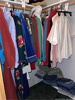 Photo shows multiple women's clothing items hanging on closet rod including a teddy bear patterned robe, various colorful tops and jackets, and folded jeans on shelf below.