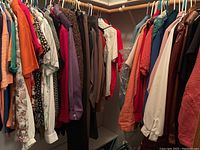 Photo showing a rack of women's clothing items including blouses, sweaters, jackets, and slacks in medium to large sizes, variety of colors and patterns.