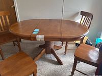 Oval wood dining table with four wooden chairs around, showing table top and leg design.