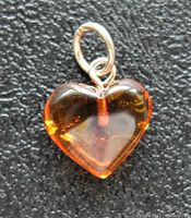 Front close-up photo of heart-shaped amber pendant with silver bail on textured black background.
