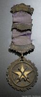 Front view of the 1923 Edmonton Freemason jewel medal showing the metal star and crossed tools design, circular border, and attached purple fabric ribbon with upper metal bar labeled 'J. DUNN'.