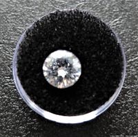 Top view photo of the clear round-cut cubic zirconia gemstone in a plastic container on black velvet.