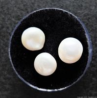 Top view of three genuine freshwater pearls on black felt with clear round container base.