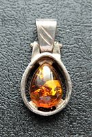 Front view of solid sterling silver pendant with teardrop-shaped amber stone showing natural inclusions and warm orange hues.