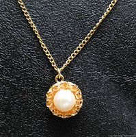 Close-up of the pearl pendant with gold floral design.