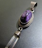 Close-up of front of pendant showing oval purple gemstone set in textured sterling silver bezel with hanging clear quartz crystal