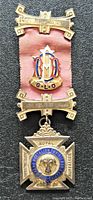 Front view of the freemason jewel medal with pink ribbon, gold enamel emblem "G.L.O.", and a Maltese cross with a lion head at center and inscriptions.