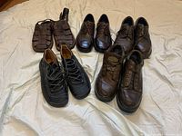 Photo showing all five pairs of men's shoes arranged on fabric background including dark woven sandals, two pairs of brown lace-up shoes, black lace-up boots and worn brown boots without laces.
